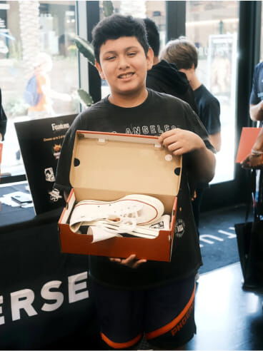 A young man holding a box with a pair of Converse inside of it